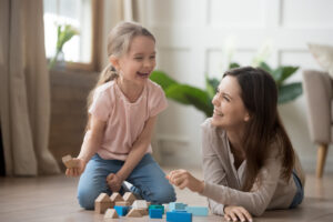 happy mom and kid daughter laughing playing with wooden blocks