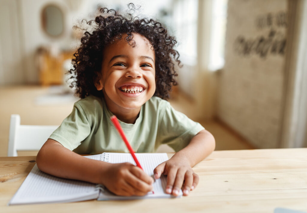 smiling african american child school boy doing homework while sitting at desk at home