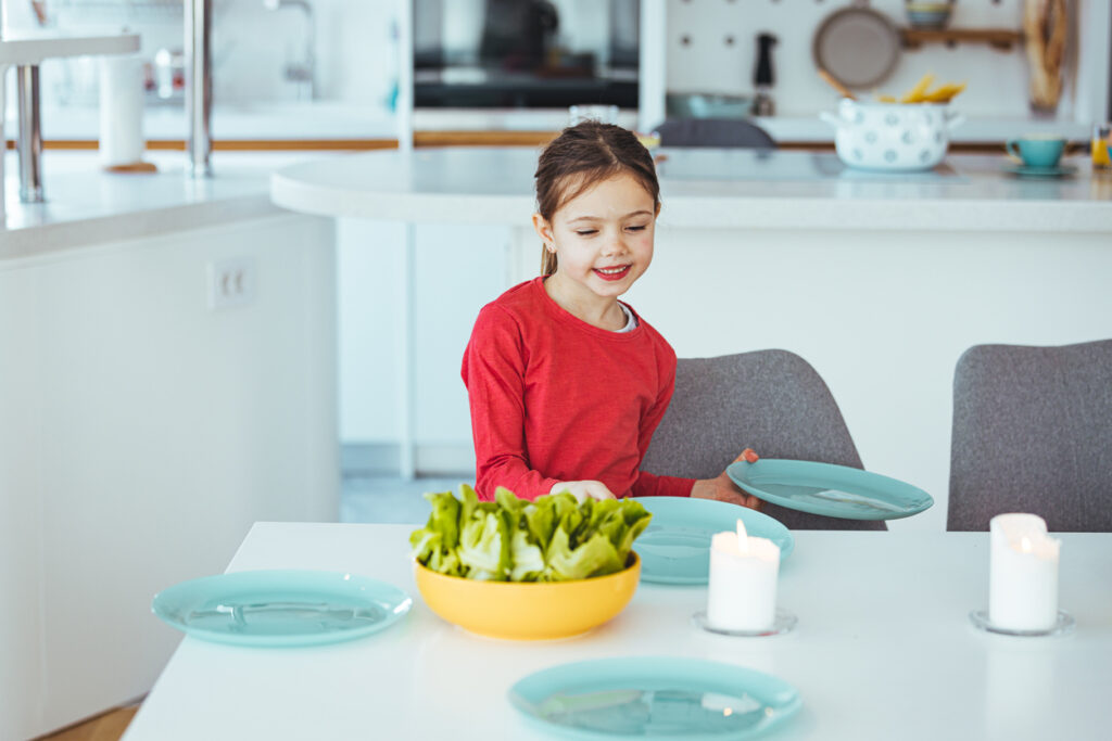 a young girl helps to set the family dining room table.