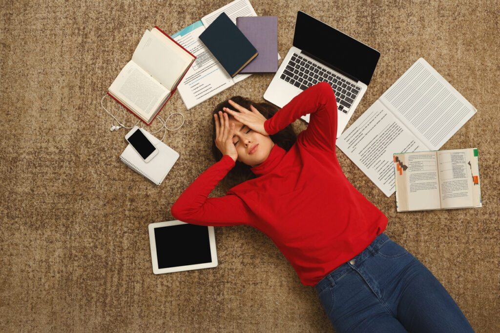 tired student girl lying on the floor with books and gadgets