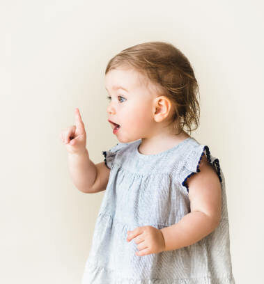 baby girl pointing her finger, excited and emotional, on neutral background