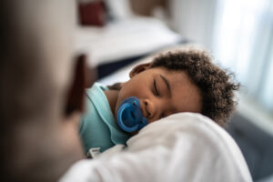 father putting baby son to sleep on his arms at home