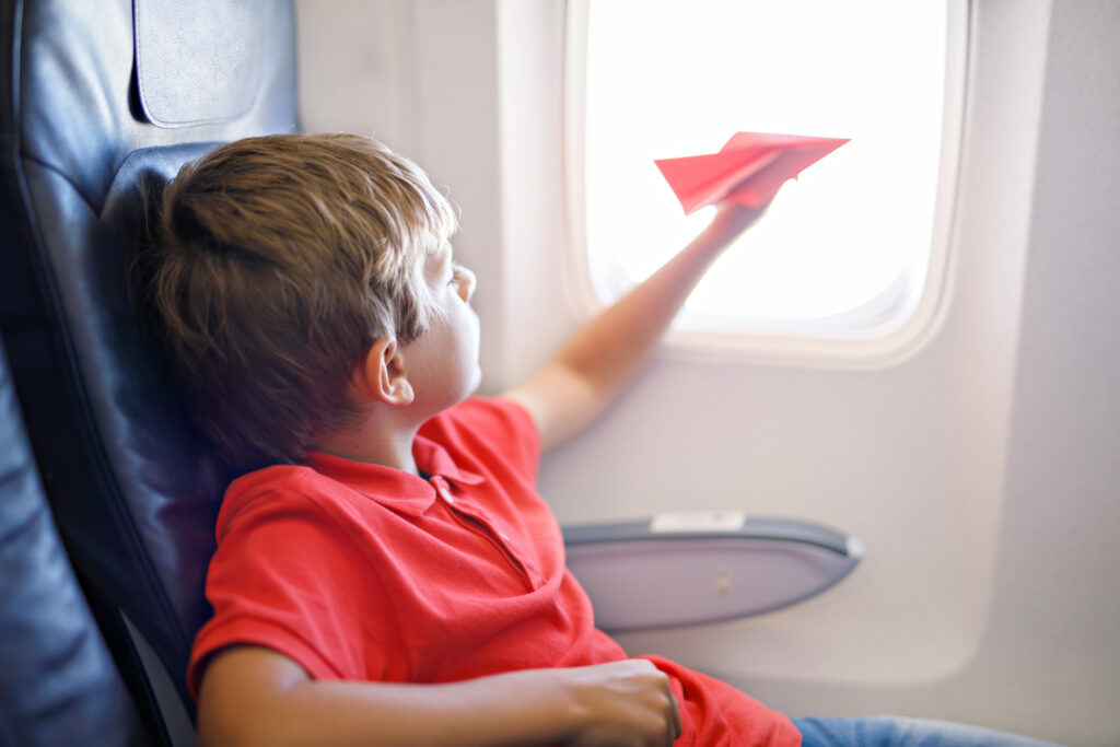 little kid boy playing with red paper plane during flight on airplane