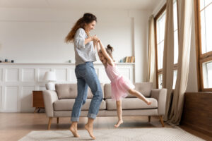 happy young mum and little daughter dancing at home