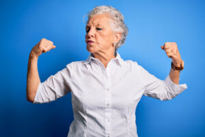 senior beautiful woman wearing elegant shirt standing over isolated blue background showing arms muscles smiling proud. fitness concept.