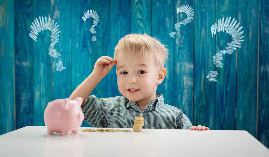 three years old child sitting at the table with money coins and piggybank