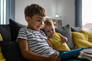 one boy sitting with little sister at home looking at digital table