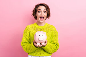 conceptual photo of young amazed funny girl shocked celebrate finish dream achievement hold piggy bank isolated on pink color background