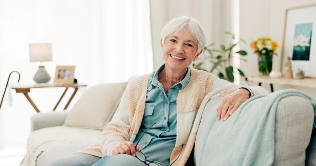 happy, senior woman and relax on sofa in nursing home or grandma with happiness, freedom and retirement in house. portrait, elderly person and smile in living room or thinking of good memory