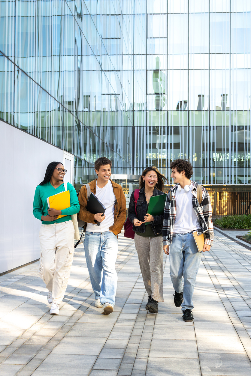 vertical image of multiracial happy university students walking to class together laughing and talking.