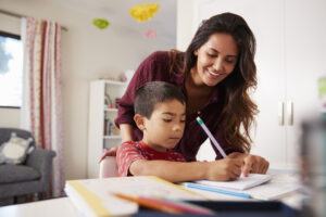 mother helping son with homework sitting at desk in bedroom