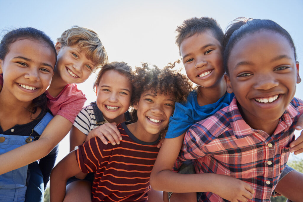 six pre teen friends piggybacking in a park, close up portrait