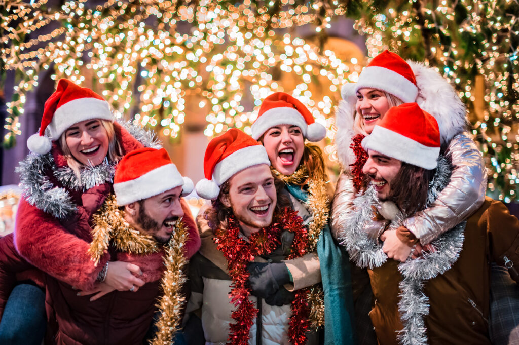 happy group of friends wearing santa claus hat and celebrating christmas night together young people having fun during winter holidays teenagers celebrating new year's eve in front of tree