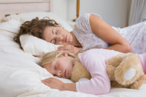 girl and mother sleeping with stuffed toy in bed