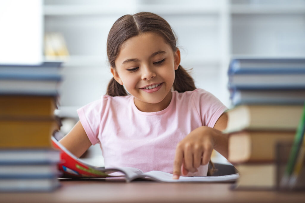 the happy schoolgirl sitting at the desk with books