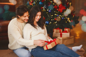 pregnant woman and her husband opening xmas gifts