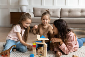 happy young mother playing with two daughters on warm floor