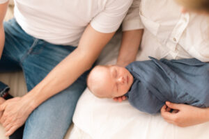 close up of parents holding newborn baby son wrapped in swaddle blanket at home.