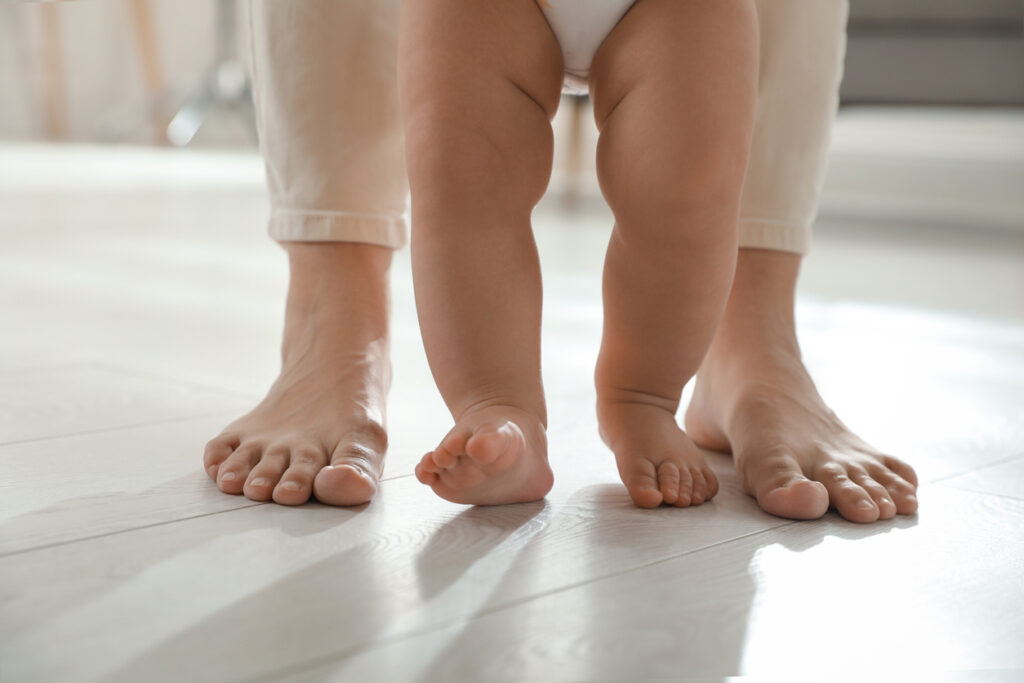 mother supporting her baby daughter while she learning to walk at home, closeup