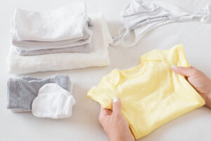 woman's hands sorting new baby clothes on white bed sheet. mother's daily duties. soft colors. closeup.
