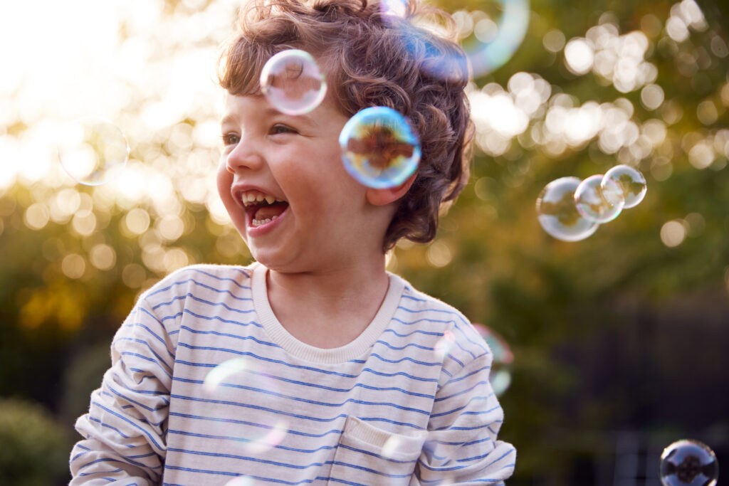 young boy having fun in garden chasing and bursting bubbles