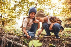 two little kids in warm hats with backpacks examining tree bark
