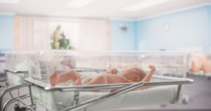 adorable caucasian newborn child lying in hospital bed in a nursery clinic. little playful and healthy baby. medical health care, maternity and parenthood concept