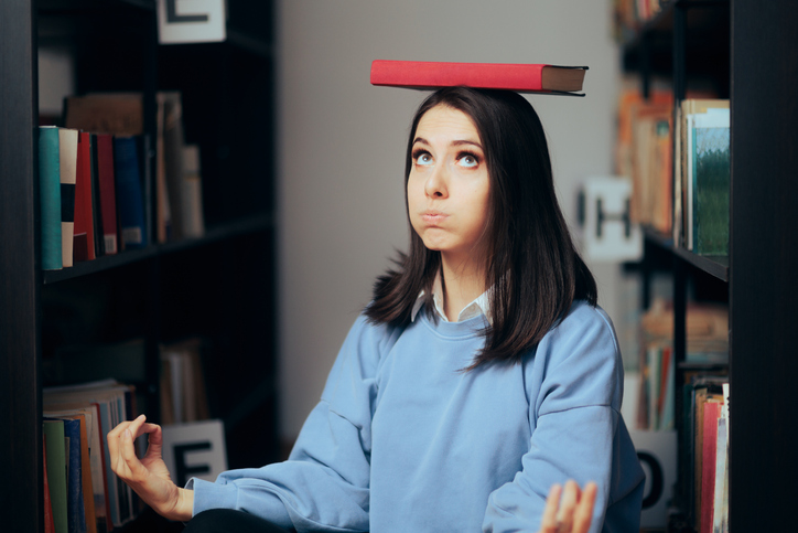studious woman balancing a book on her head sitting in a library