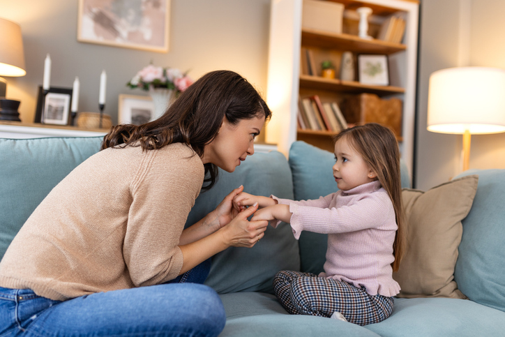 a young family shares a tender moment. a child daughter holding their mother's arms, both smiling with love and joy. they relax on the living room sofa, cherishing quality time together.